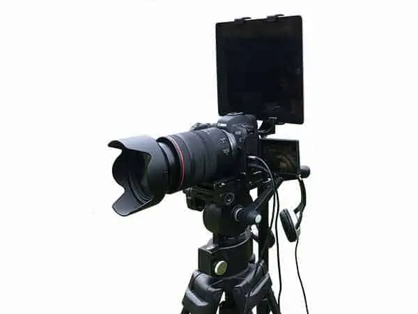 An iPad running is mounted on a light stand and placed immediately behind, and a little above, the camera. If the presenter moves about 6-10ft back from the camera he/she can read the script on the iPad while appearing to be looking into the camera lens.