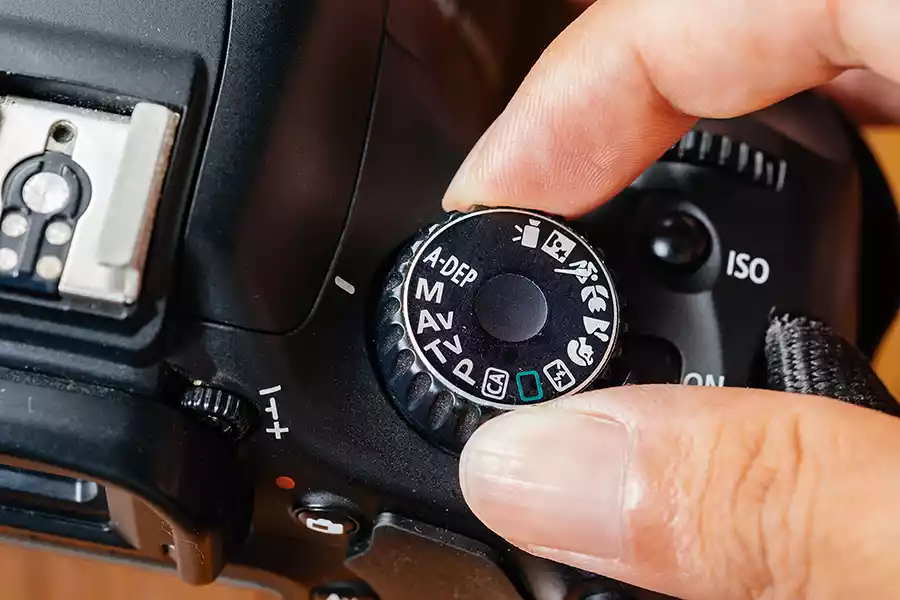 Photographer using the camera mode dial on a DSLR