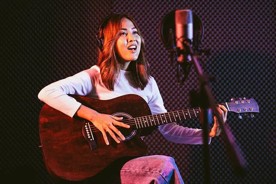 Girl playing guitar and singing into a microphone with a pop filter